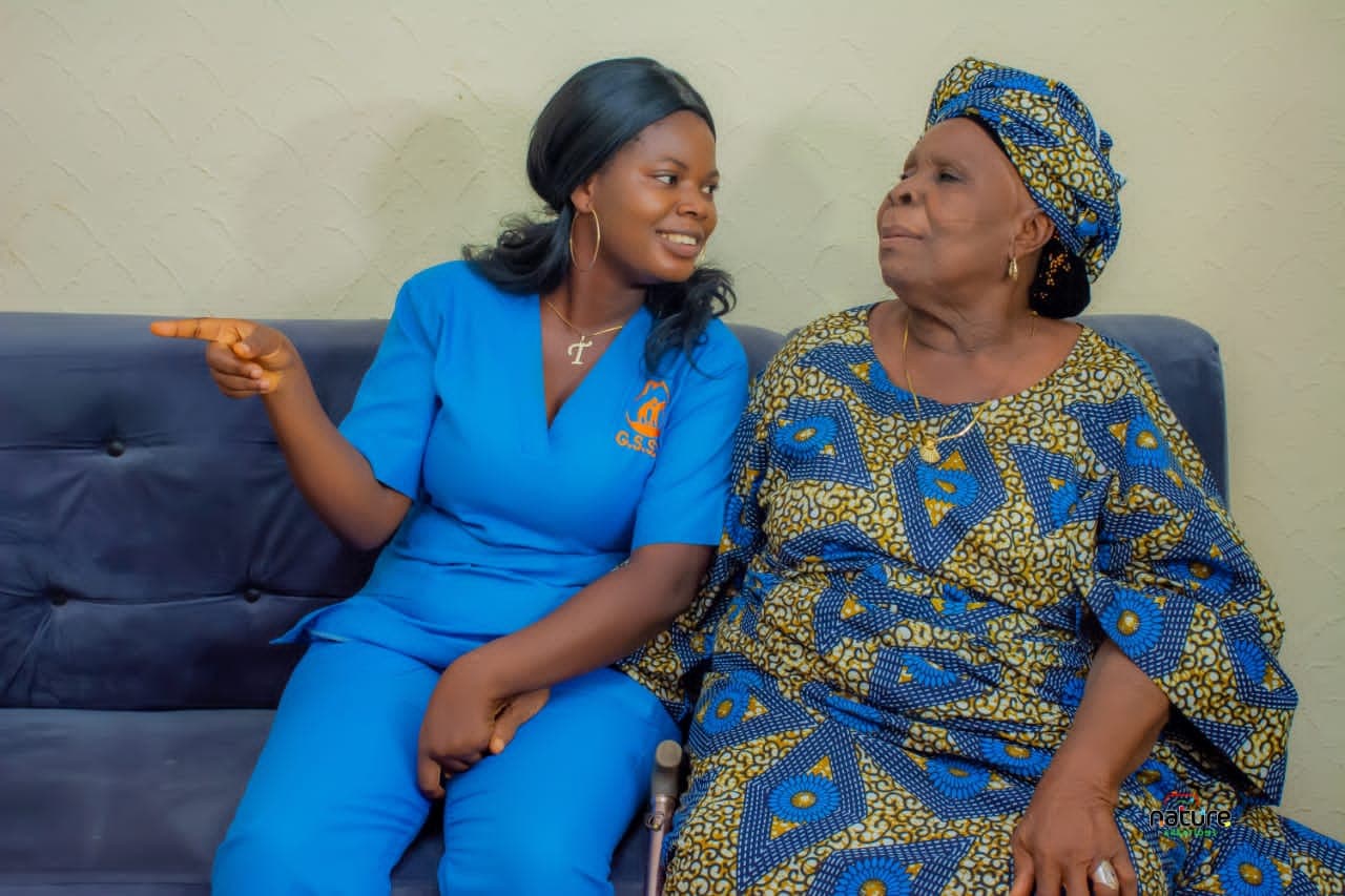 A caregiver in blue sitting with an older woman at Grace Senior Social Care